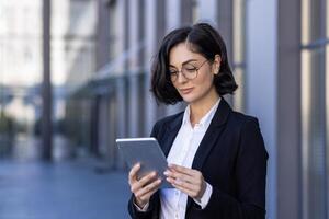 Close-up photo of serious young businesswoman talking on the street near work office on call on tablet, watching and developing project, startup, waiting for meeting.