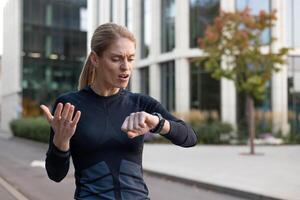 Frustrated female runner checking smartwatch time, late for meeting, urban background, active lifestyle concept photo