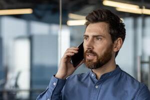 Close-up photo of a young businessman, programmer talking on the phone while standing in the office.