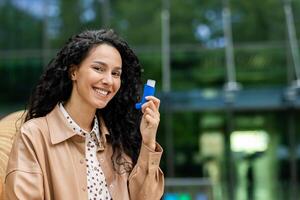 sonriente caucásico hembra participación azul inhalador cerca a cara en antecedentes de verde zona y moderno edificio. hermosa mujer haciendo respiración más fácil mientras utilizando nebulizador en Fresco aire. foto