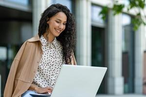 Portrait of a smiling young professional woman using a laptop in an urban outdoor setting, exuding confidence and positivity. photo