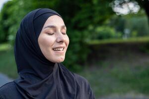 de cerca de un contenido joven mujer vistiendo un hiyab, ojos cerrado con un tranquilo expresión, rodeado por verdor en un sereno ambiente. foto