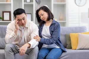 familia psicológico apoyo, asiático Pareja sentado a hogar en sofá considerado, mujer consolador y secundario Deprimido hombre. foto