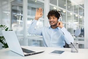 contento joven adulto en un moderno oficina ajuste olas Hola mientras escuchando a música mediante auriculares, exudando un relajado, alegre atmósfera. foto