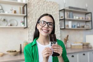 retrato de un mujer participación un bar de negro chocolate en su manos. en pie a hogar en el cocina foto