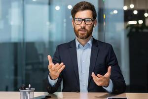 un joven hermoso empresario hombre conduce negocio formación en línea. él se sienta en el oficina en frente de el cámara, enseña, consultas. foto