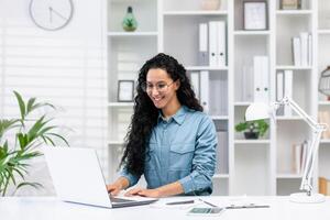 sonriente Hispano mujer enfocado en trabajo a su hogar oficina, exudando profesionalismo y confianza en un brillante ajuste. foto
