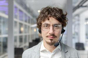 Adult male office worker with a headset appears concentrated and experienced in a bright modern office. Emotionally engaged and professional. photo