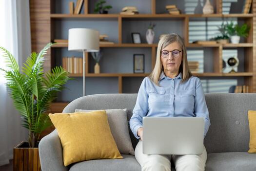 profesional mujer sentado en un sofá, comprometido en remoto trabajo en su ordenador portátil en un acogedor vivo habitación. foto