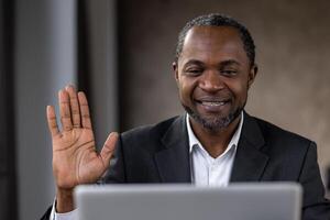 A man in a suit is smiling and waving at the camera. He is wearing a white shirt and a black jacket photo