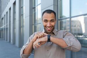 Young handsome Hispanic African American businessman talking on smart watch near the office center photo