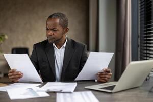 A man in a suit is holding two pieces of paper in his hands, looking at them with a frown on his face photo