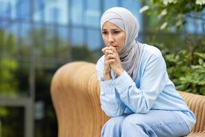 Depressed female in headscarf leaning on laps with elbows while sitting deep in thoughts with worried face. Sad lady feeling lonely and unhappy while waiting for appointment with psychotherapist. photo