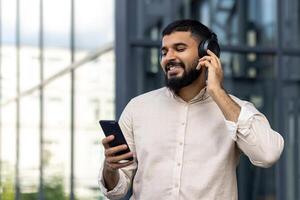 sonriente barbado hombre disfrutando música en auriculares al aire libre foto