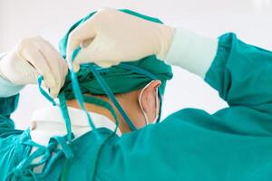 Back view of surgeon tying surgical cap in preparation, Medical team performing surgical operation in operating room, Team surgeon at work in operating room photo