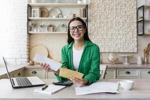 Happy and successful business woman working at home in kitchen, looking at camera photo