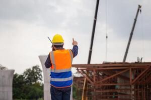 capataz trabajador comprobación proyecto a edificio sitio, ingeniero, y constructores en sombreros duros en construcción sitio foto