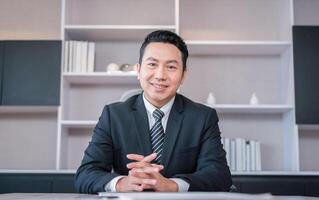 Asian businessman sitting at office desk and looking at camera photo