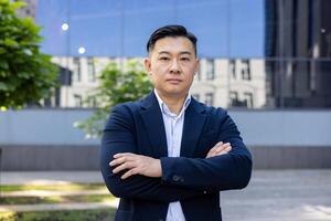 Portrait of a professional Asian businessman with crossed arms, exuding confidence against a modern city backdrop. photo