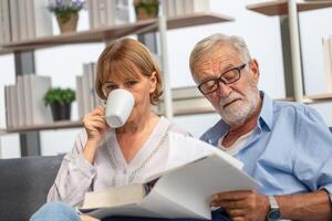 Senior couple spending time together in the living room, woman and man reading a book and enjoying coffee on the cozy sofa at home photo