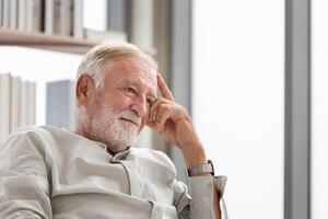 Thinking senior man sits on a couch in the living room, Elderly man thinks and sit on the sofa photo