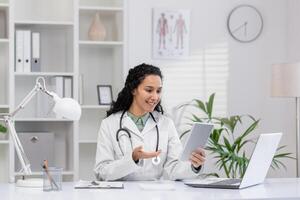 un profesional hembra médico en un blanco Saco usos un tableta para telemedicina consulta en su brillante oficina, simbolizando cuidado de la salud innovación y paciente cuidado. foto