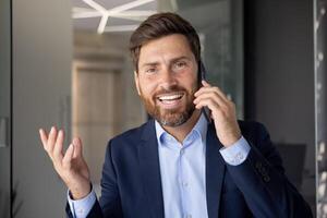 de cerca retrato de un contento y sonriente joven empresario en pie en el oficina y hablando en el móvil teléfono, mirando a el cámara con un sonrisa. foto