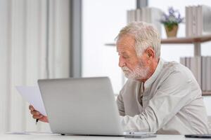 un anciano preocupado revisando sus facturas, una familia anciana jubilada leyendo documentos, un hombre maduro en la sala de estar con una laptop foto