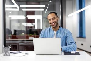 Happy young professional works on computer with a smile, in a bright contemporary workspace. Represents job satisfaction and a positive work environment. photo