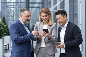 Tres colegas empleados reloj gracioso s o Mira a fotos, imágenes recuerdos mirando a teléfono inteligente pantalla utilizando móvil teléfono. grupo de negocio personas oficina trabajadores teniendo divertido en rompe foto