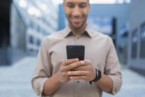 Close up photo selective focus african american man typing message on phone smiling and happy businessman using smartphone