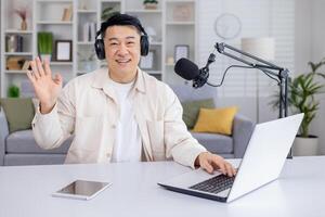 A cheerful male podcaster is greeting viewers with a wave while recording a live podcast session at his home studio setup. photo