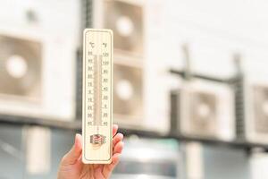 Hot temperature, Hand holding thermometer with blurred air conditioner compressor photo