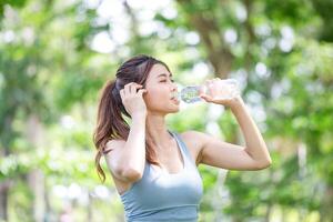 joven aptitud mujer vistiendo Deportes ropa Bebiendo Fresco agua, hermosa asiático niña en ropa de deporte Bebiendo agua desde un botella foto