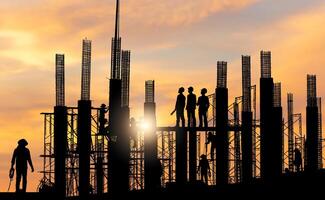 Silhouette of Engineer and worker checking project at building site background, construction site at sunset in evening time photo