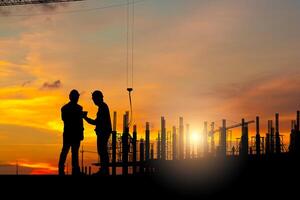 silueta de ingeniero y trabajador equipo comprobación proyecto a edificio sitio fondo, un construcción sitio con puesta de sol foto