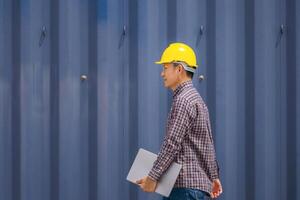 Engineer man with laptop in industry containers cargo, Foreman dock worker in hardhat and safety vest control loading containers box from cargo photo