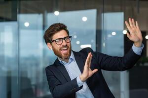 Mature successful manager boss celebrating good achievement and good work result, man dancing at workplace inside office, businessman at work in business suit. photo