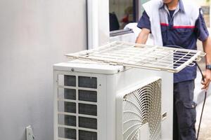 Selective focus of Air conditioner compressor with blurred technician man cleaning air conditioner in background, Repairman washing dirty compartments air conditioner photo