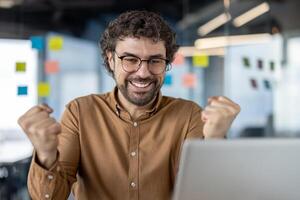 Euphoric business professional triumphantly raising fists in a jubilant gesture of success and achievement at the workplace. photo