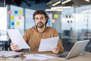 Professional male entrepreneur examining papers with concentration, surrounded by technology and planning tools in a contemporary workspace. photo