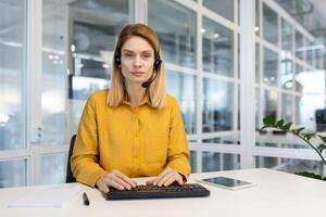 Web view camera, pov. Woman with a headset phone listens to the interlocutor, call, online meeting. The support service worker looks seriously and thoughtfully at camera, works inside office. photo