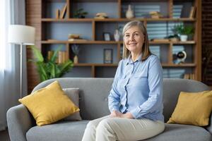 Portrait of a relaxed mature woman smiling and sitting comfortably on a couch with stylish interior background. photo