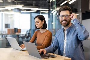 un hombre y mujer trabajo lado por lado en un brillante, moderno oficina configuración, ambos utilizando laptops y mostrando un positivo, enfocado actitud. foto