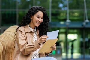 A young woman engrossed in reading a letter sits comfortably outdoors with a lush green background. This image evokes a sense of communication, relaxation, and the beauty of nature. photo