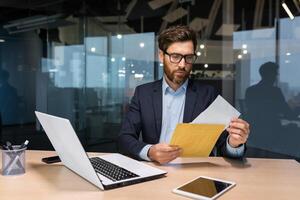 Mature and serious businessman inside office thoughtfully reading letter received notification, man in business suit investor at work using laptop. photo