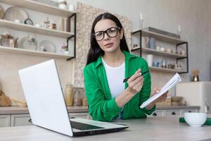 A worried young woman sits at home jots down the family budget in a notebook, counts, bills photo