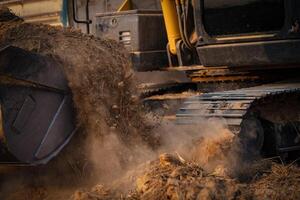 Selective focus on metal bucket teeth of backhoe digging soil. Backhoe working by digging soil at construction site. Crawler excavator digging on soil. Earth moving machine. Excavation vehicle. photo