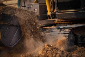 Selective focus on metal bucket teeth of backhoe digging soil. Backhoe working by digging soil at construction site. Crawler excavator digging on soil. Earth moving machine. Excavation vehicle. photo