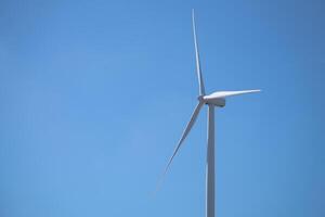 Wind turbine is standing tall in blue sky, Wind energy. Wind power. Sustainable, renewable energy. Wind turbine generate electricity. Sustainable resources. Green technology for energy sustainability. photo